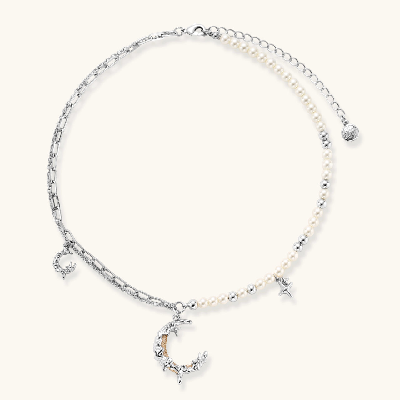 Silver-toned crescent moon pendant with star accents on pearl and chain necklace against white background.