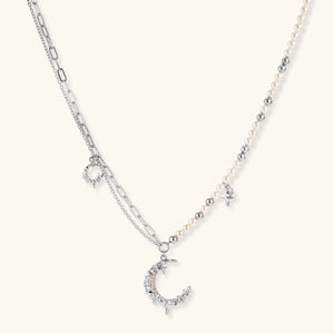 Silver-toned crescent moon pendant with star accents on pearl and chain necklace against white background.