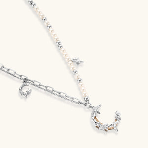 Silver-toned crescent moon pendant with star accents on pearl and chain necklace against white background.