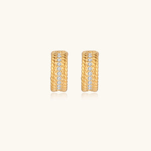 Textured gold huggie hoop earrings with raised ribbed rows creating dimensional sculptural design on cream background